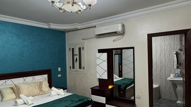 A bedroom with a bed, a dresser, a mirror, an air conditioning unit, and a bathroom door. - Cozy3-bedroom in perfect apartment   view of Pyramids ofGiza Governorate with AC (Giza Governorate)