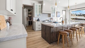 A modern kitchen with a large island, bar stools, and a view of a snowy landscape through the windows. - Summit View Lodge, 5br5ba, Sleeps 16, HotTub-Views (Heber City)