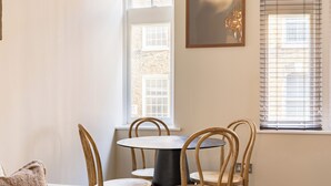 Un coin repas avec une table ronde et quatre chaises en bois, une fenêtre avec des stores et un lustre.