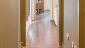 Un couloir au plancher de bois mène à une pièce dotée d’une fenêtre et d’une petite table.