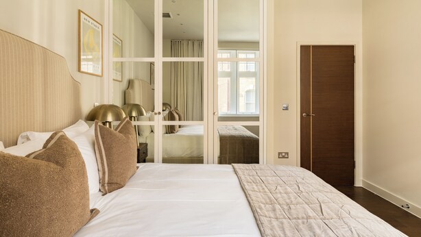 Une chambre d’hôtel avec un grand lit, une armoire avec un miroir, une table de chevet avec une lampe et une porte.