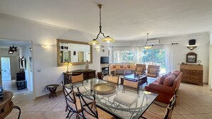 Ett rymligt vardagsrum med ett glasbord, bekväma sittplatser och ett stort fönster med utsikt över omgivningarna.