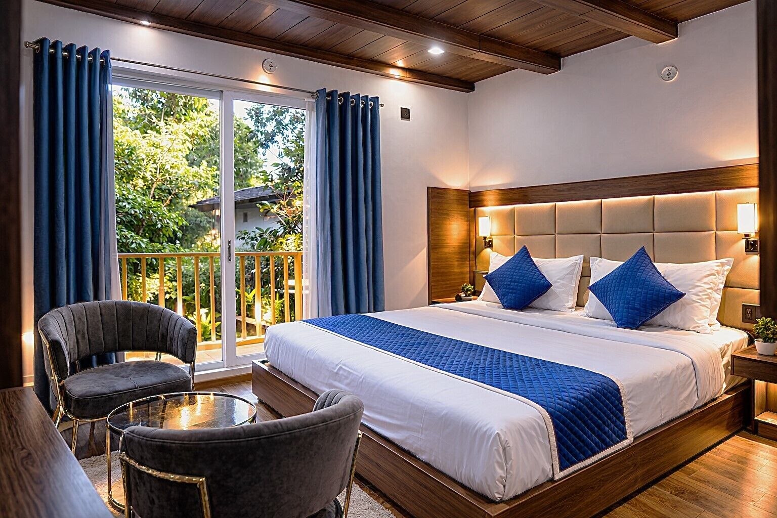 Camera d'albergo con un letto grande, due sedie, un tavolino e un balcone con tende.