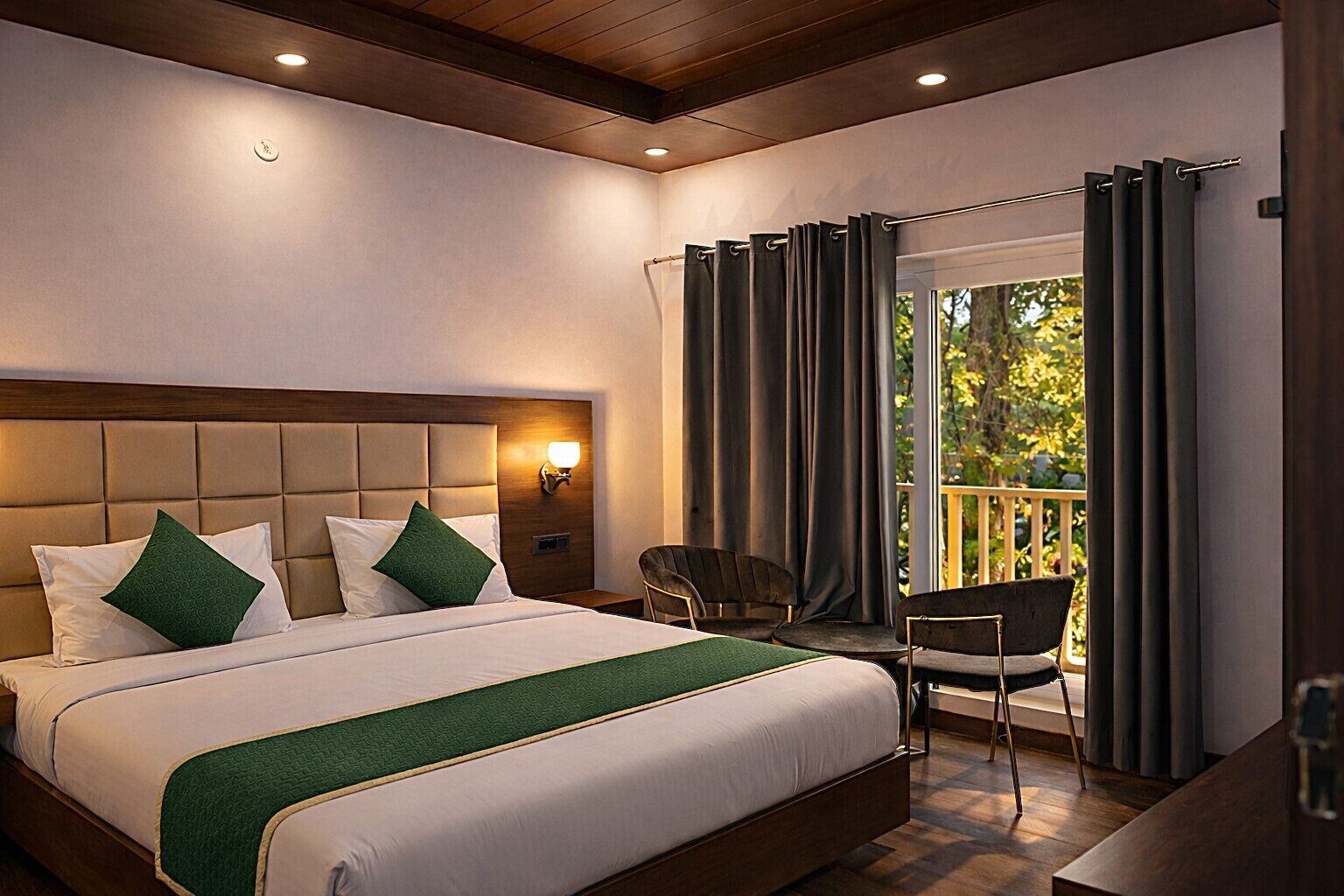 Habitación de hotel con una cama grande, una mesita de noche con lámpara, una silla y un balcón con cortinas.