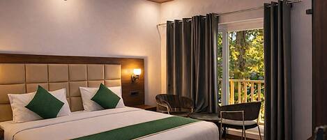 Habitación de hotel con una cama grande, una mesita de noche con lámpara, una silla y un balcón con cortinas.