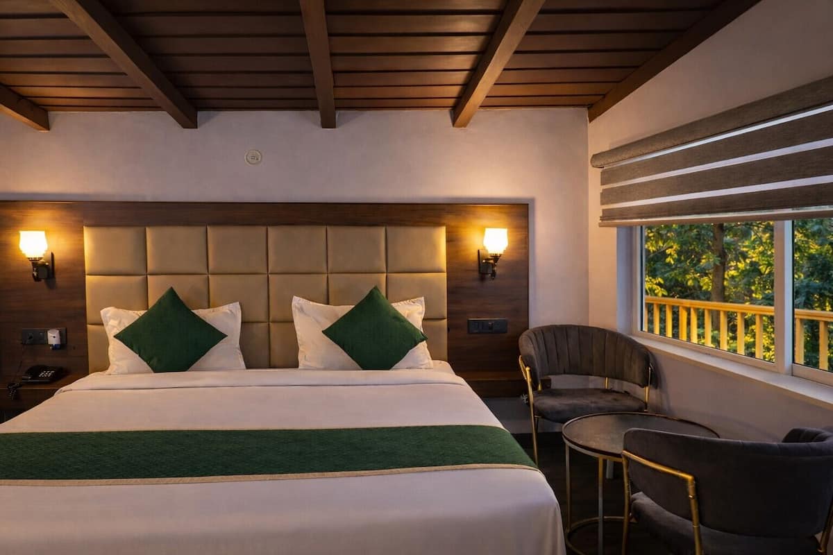 Ein Hotelzimmer mit einem großen Bett, zwei Nachttischlampen, einem Sessel und einem Fenster mit Blick auf Bäume.