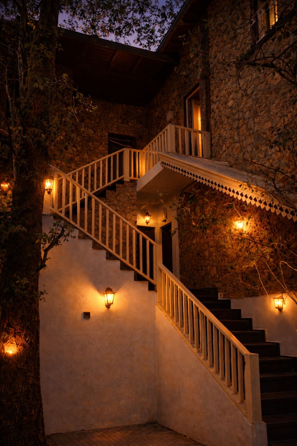 A stone staircase with white railings and wall-mounted lights, leading to an upper level.