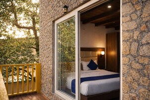 Un dormitorio con pared de piedra, un ventanal grande y un balcón con barandilla amarilla.