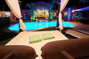 Een terras bij het zwembad met een ligbed, twee groene handdoeken en een gazebo op de achtergrond.