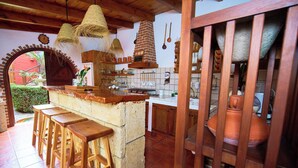 Une cuisine rustique avec un four en briques, des tabourets en bois et des pots en terre cuite.