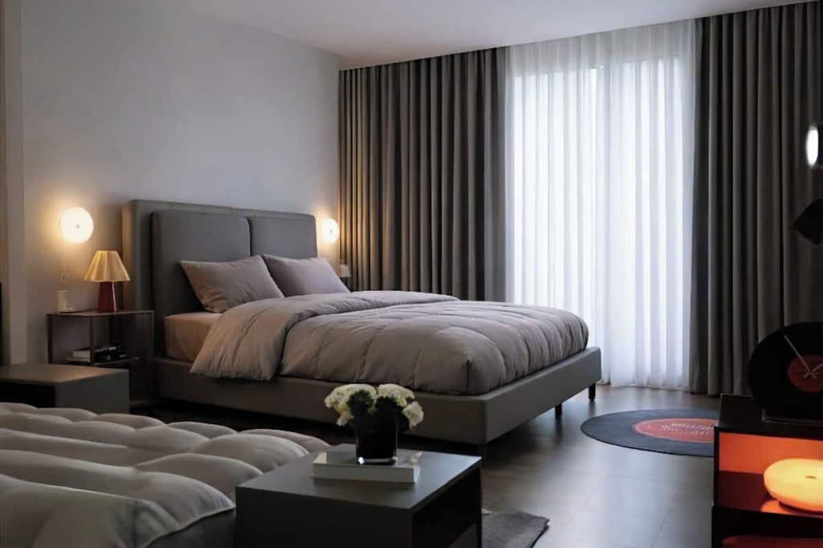 Un dormitorio moderno de hotel con una cama grande, mesitas de noche, una pequeña mesa con un florero y un tocadiscos.