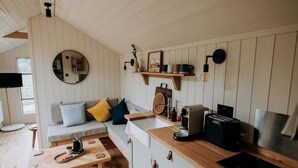A cozy kitchen with a wooden countertop, a built-in oven, and a coffee machine. There is a round mirror on the wall and a shelf with decorative items. - Elsham Hall Bothies: Countryside Retreat with Garden Views & Free Park Access (Elsham)