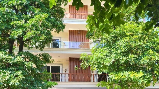 A multi-story building with balconies, a blue door, and surrounding trees. - Kommune Living (Gurugram)