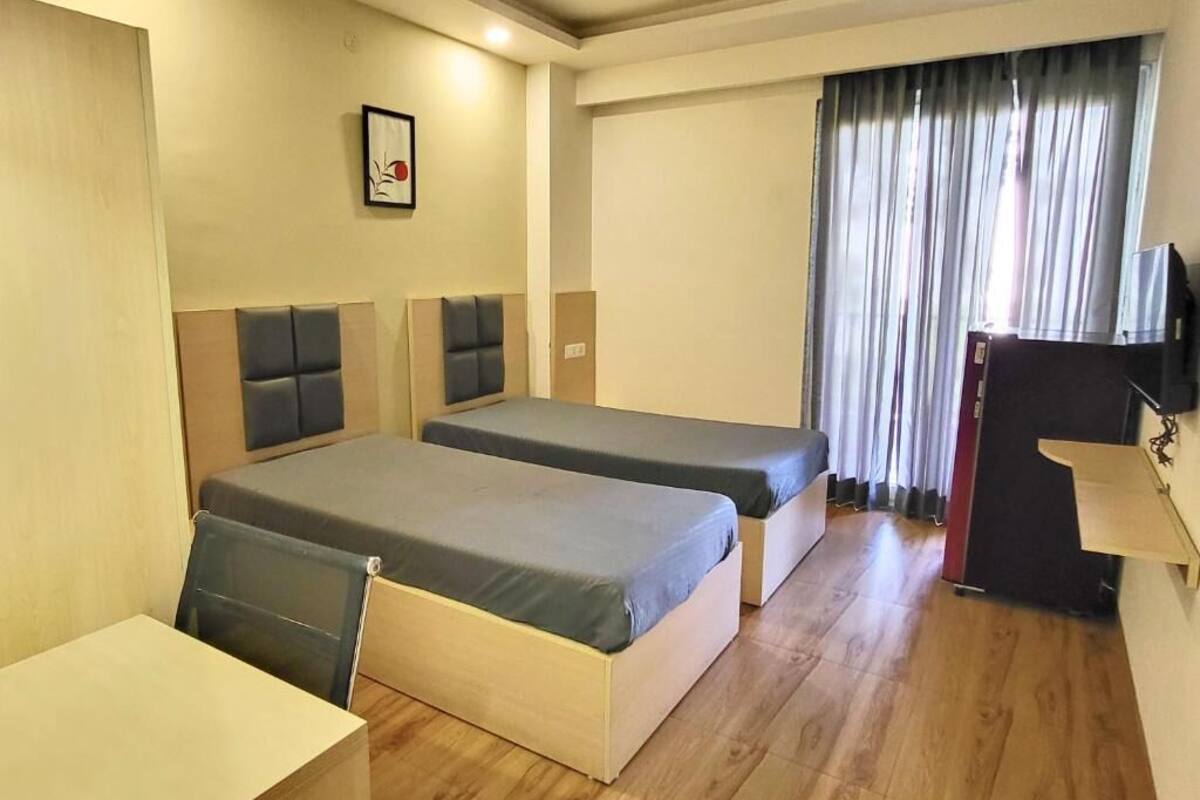 A hotel room with two single beds, a desk, a chair, a TV, and a window with curtains.