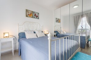 Une chambre à coucher avec un lit en métal blanc, une couvre-lit bleue et une table de chevet avec une lampe.