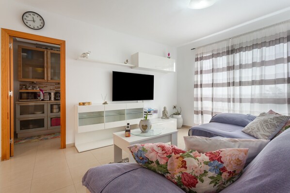 Una sala de estar moderna con una televisión de pantalla plana, un sofá, una mesa de centro y una cocina con armarios y electrodomésticos.