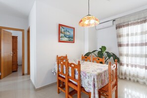 Ein Essbereich mit einem Tisch für vier Personen, Holzstühlen, einer hängenden Pendelleuchte, einem gerahmten Bild an der Wand und einer großen Pflanze.