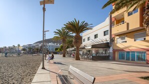 Une promenade en bord de mer avec un banc, des palmiers et des bâtiments en arrière-plan.