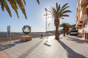 Un paseo marítimo en la playa con palmeras, una escultura de metal y una vista despejada del mar.