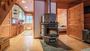 A cozy cabin interior with a central wood-burning stove, wooden walls, a kitchen area with stools, and a large window. - Snow Lodge Levi Center 8B by Aavalevi (Levi)