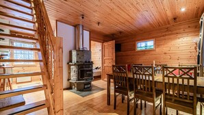 A wooden cabin interior with a central fireplace, a dining table with chairs, and a staircase. - Snow Lodge Levi Center 8B by Aavalevi (Levi)