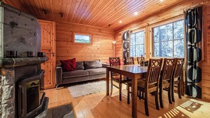 A cozy cabin interior with a fireplace, wooden walls, a sofa, a dining table with chairs, and large windows. - Snow Lodge Levi Center 8B by Aavalevi (Levi)