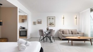 A modern hotel room with a bed, a dining area with chairs, a sofa, a coffee table, a kitchen area, and a framed picture on the wall. - By Edom - דירה נוף מטריף לים במתחם סי סייד (Eilat)