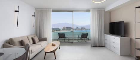 A modern living room with a sofa, dining table, chairs, a TV, and a balcony with a city view.