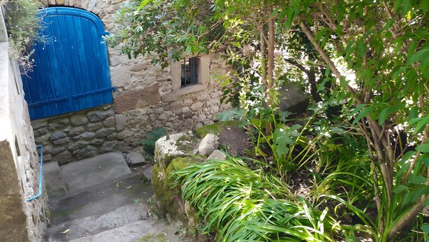 Un mur de pedra amb una porta blava, una finestra petita i una escala que baixa.