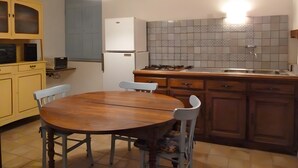 Una cuina amb una taula rodona de fusta, dues cadires, una placa de cocció i un frigorífic.