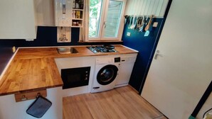 Eine kompakte Küche mit Holzarbeitsplatte, einer integrierten Waschmaschine und einem Fenster mit Jalousien.