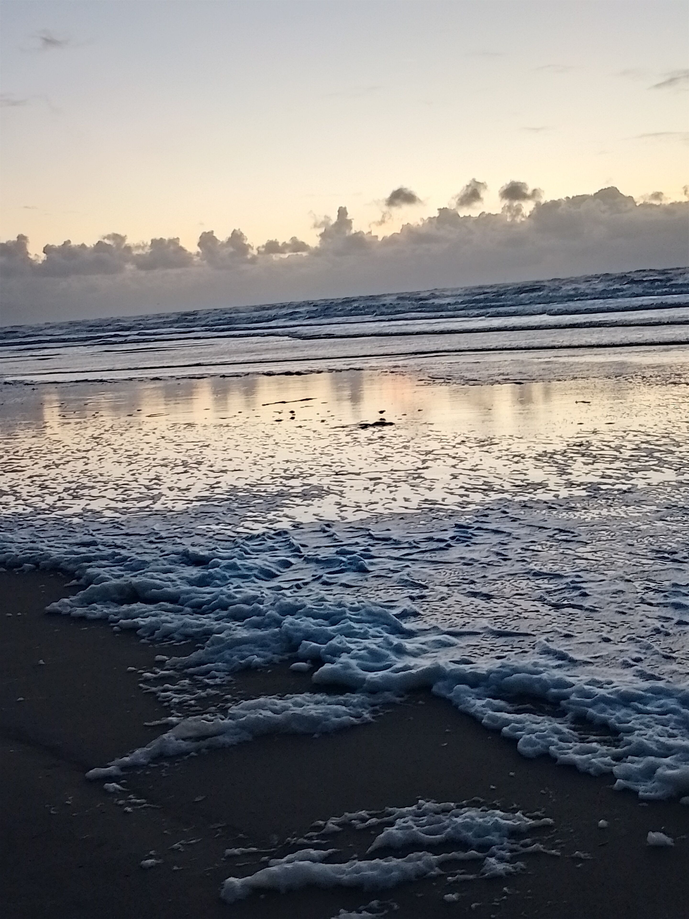 Une plage où les vagues viennent doucement lécher le rivage, sous un ciel dégagé.