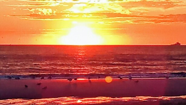 Ein Sonnenuntergang über dem Meer mit einem Strand im Vordergrund.