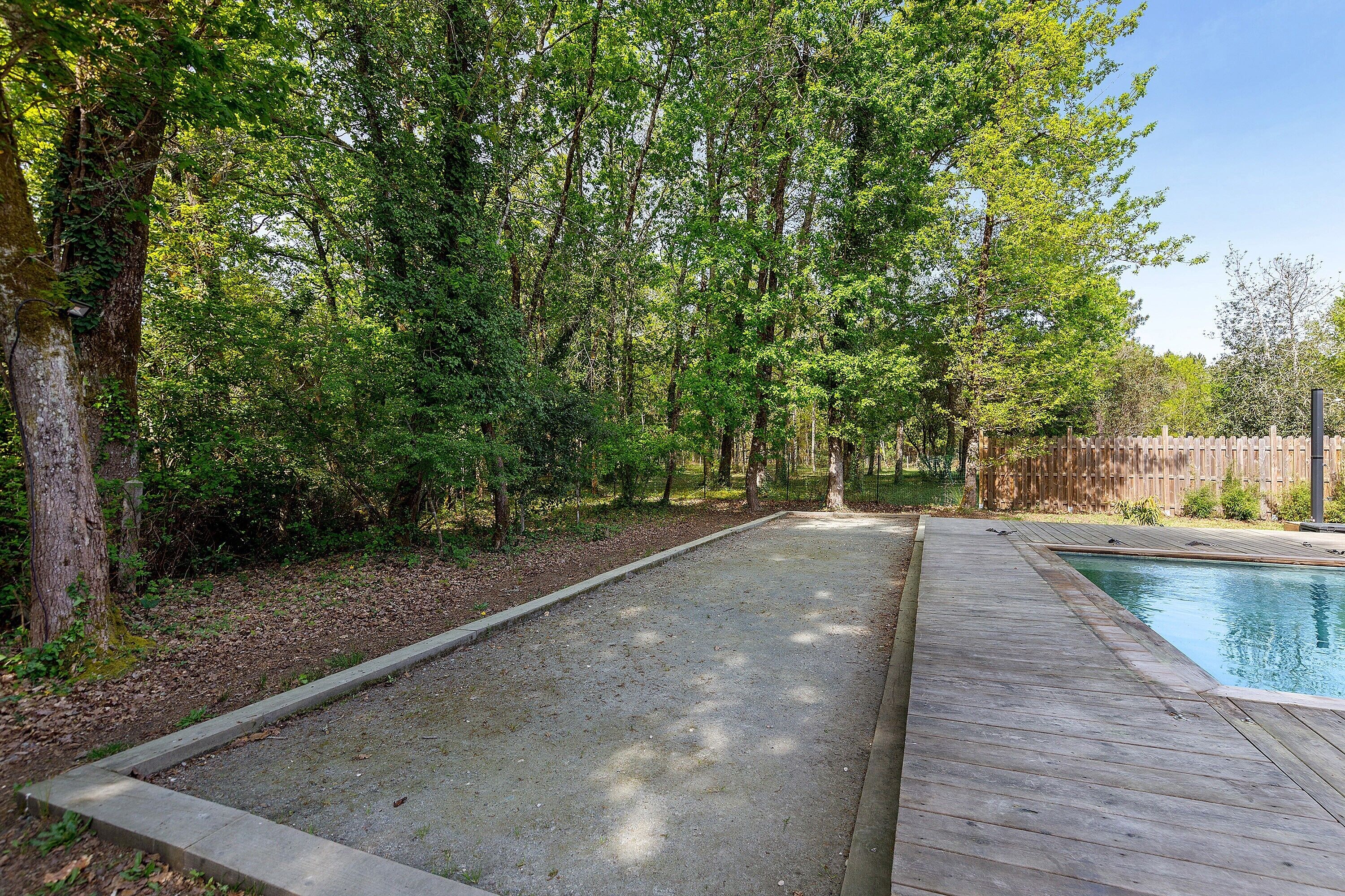 A backyard with a wooden deck, a concrete patio, and a swimming pool.