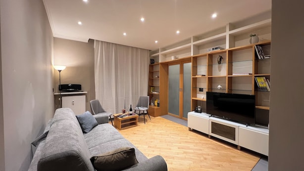A modern living room with a grey sofa, two armchairs, a coffee table, a TV, and built-in shelving with books and decorative items. - The Sixteen Suite, elegant apartment in University District, Milan. (Milano)