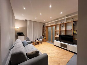 A modern living room with a grey sofa, two armchairs, a coffee table, a TV, and built-in shelving with books and decorative items. - The Sixteen Suite, elegant apartment in University District, Milan. (Milano)