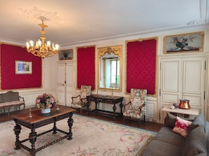 A room with a chandelier, a sofa, a table, chairs, and a mirror.