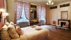 Un dormitorio con una cama grande, dos sillones, una chimenea y un espejo.