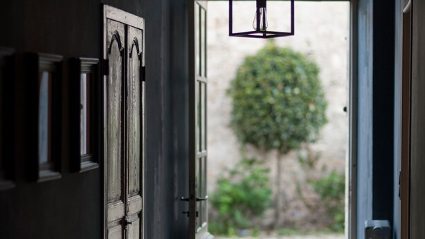 Un pasillo con una pared oscura, una puerta de madera y un candelabro colgante.