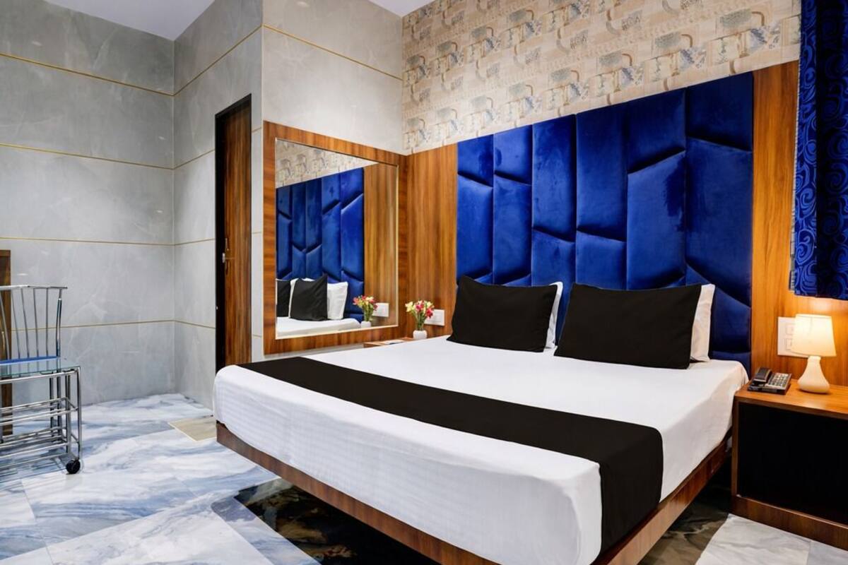 Quarto de hotel moderno com uma cama grande, cabeceira de madeira, piso de mármore e um espelho sobre a cama.