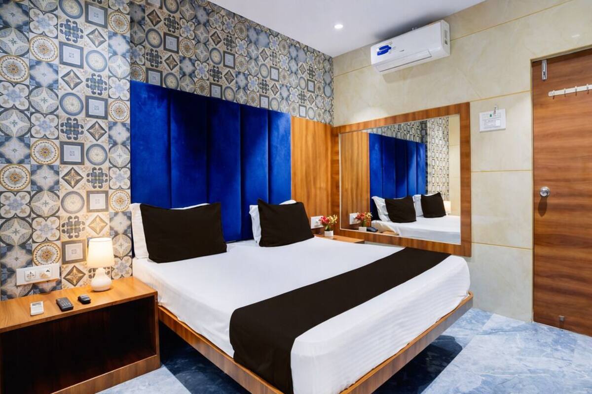 Quarto de hotel com uma cama grande, uma mesinha de cabeceira de madeira, um criado-mudo, um espelho e uma parede com padrão.