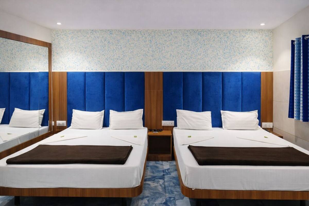 Quarto de hotel com duas camas, cabeceira de madeira, piso de mármore e um espelho em uma das paredes.
