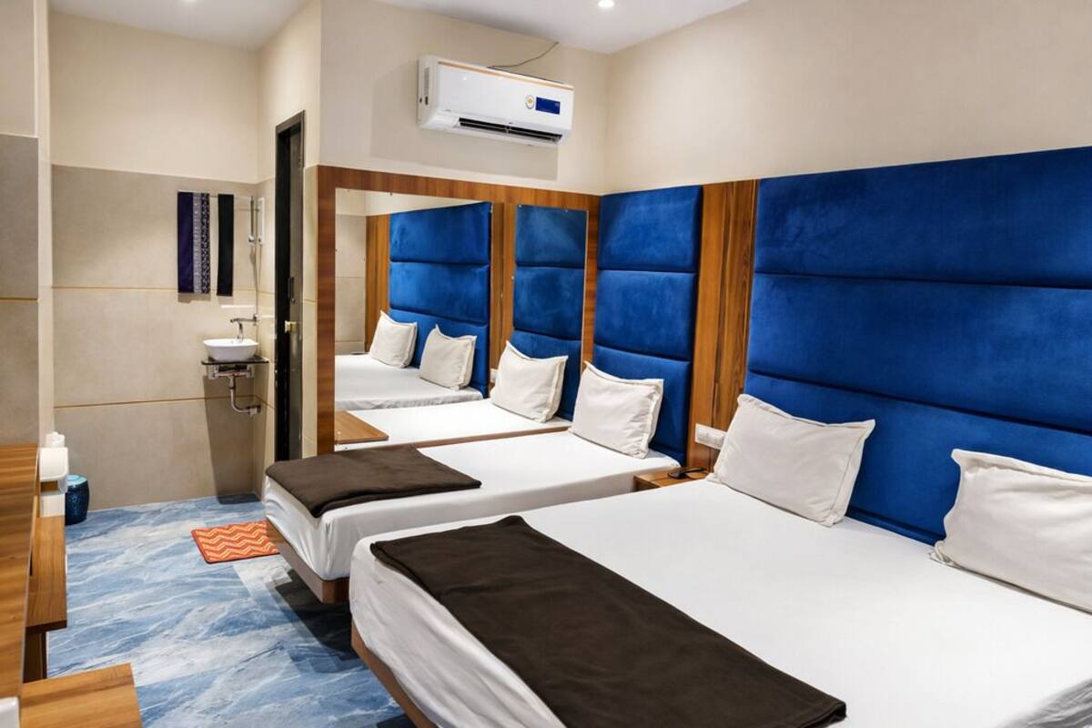 Quarto de hotel com três camas, banheiro e ar condicionado.