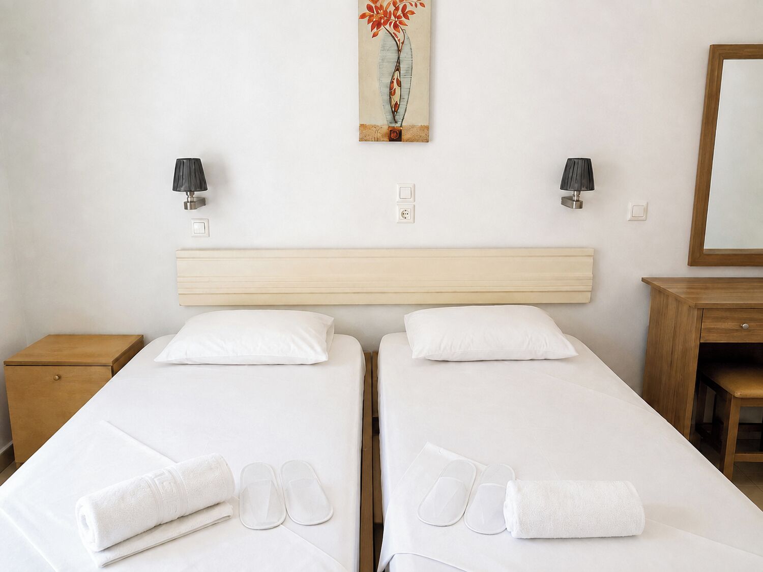 A hotel room with two beds, a wooden headboard, bedside lamps, a painting, and a mirror.