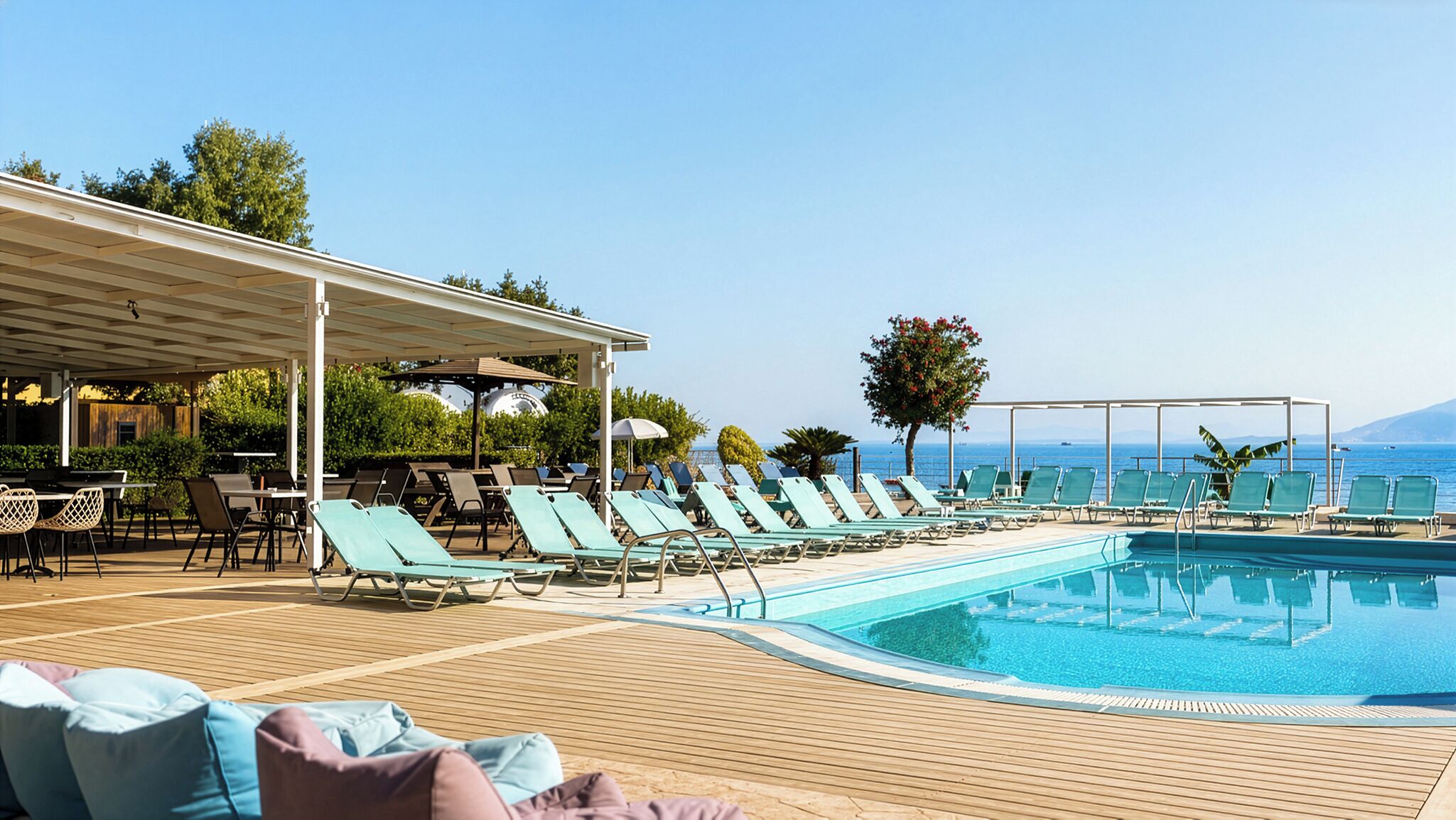 A poolside area with lounge chairs, a covered seating area, and a view of the sea.
