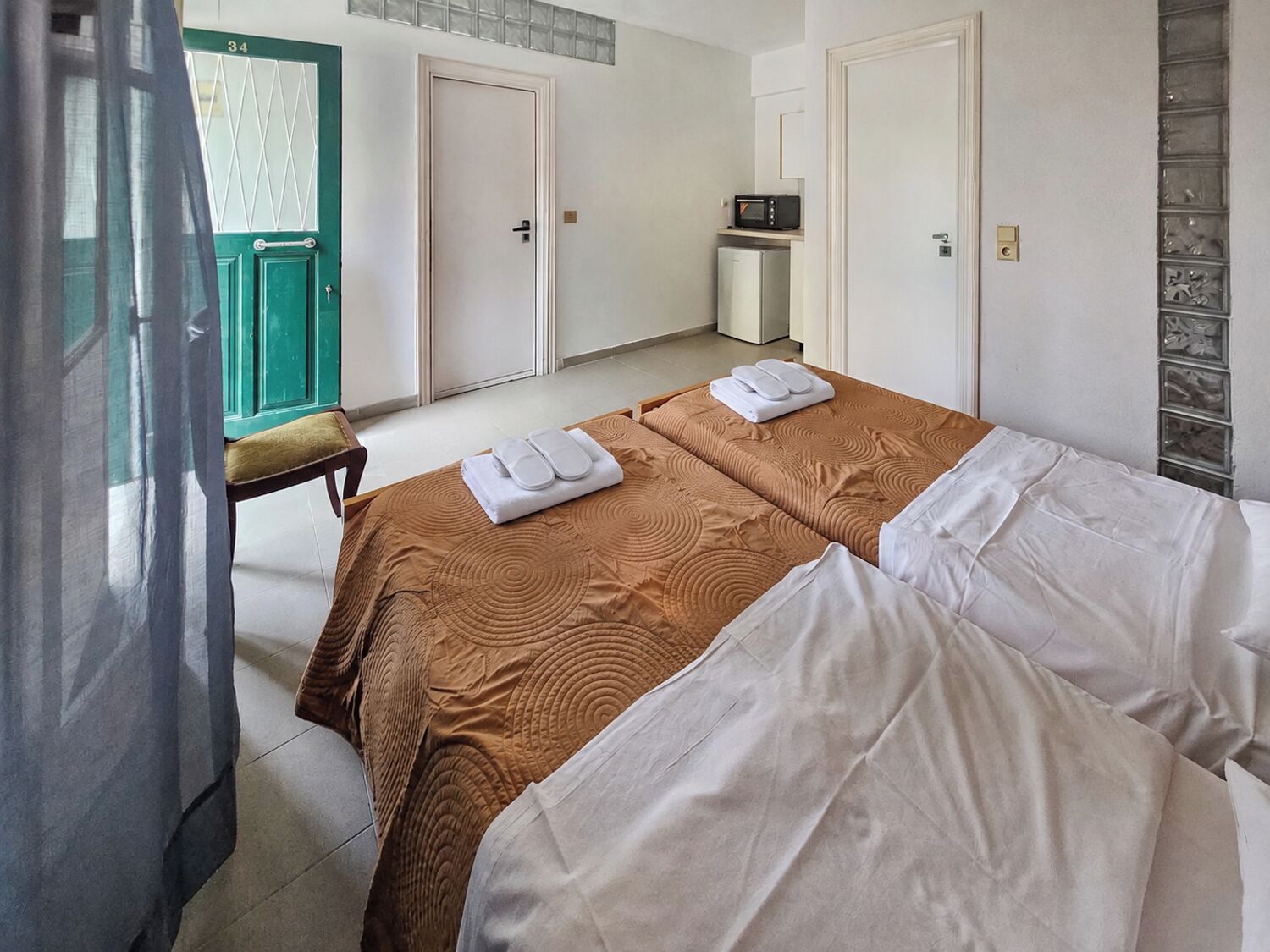 A hotel room with two beds, a microwave, a small refrigerator, and a green door.