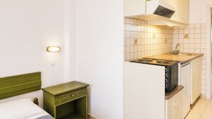 Ein gemütlicher Raum mit Bett, Nachttisch, einer Küchenzeile mit Herd und Spüle.