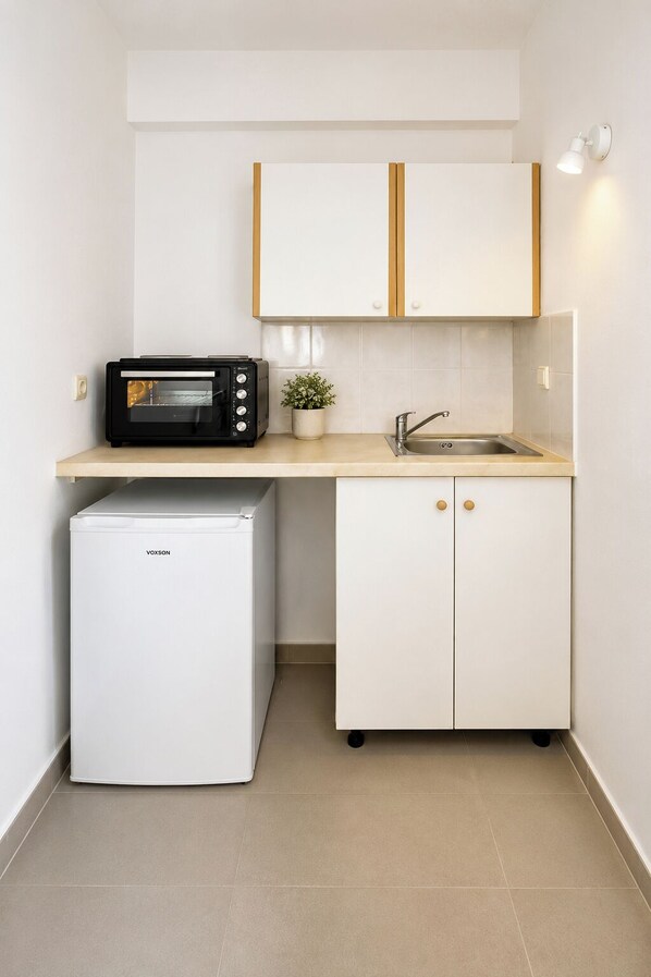 Een kleine keuken met een magnetron, een koelkast, een spoelbak en een kastje.