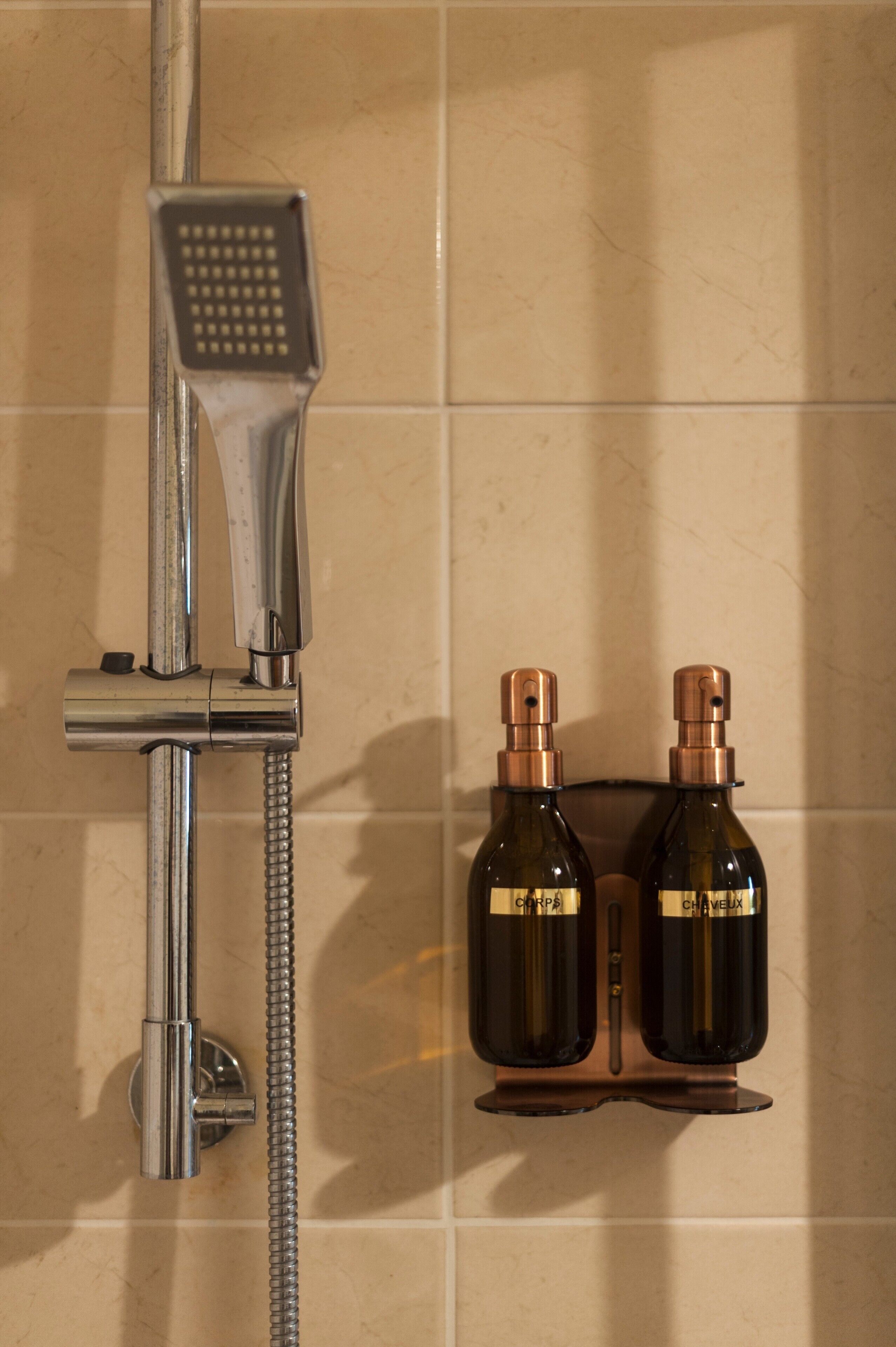 A shower with a handheld showerhead and a wall-mounted faucet, two bottles of shampoo, and a towel rack.