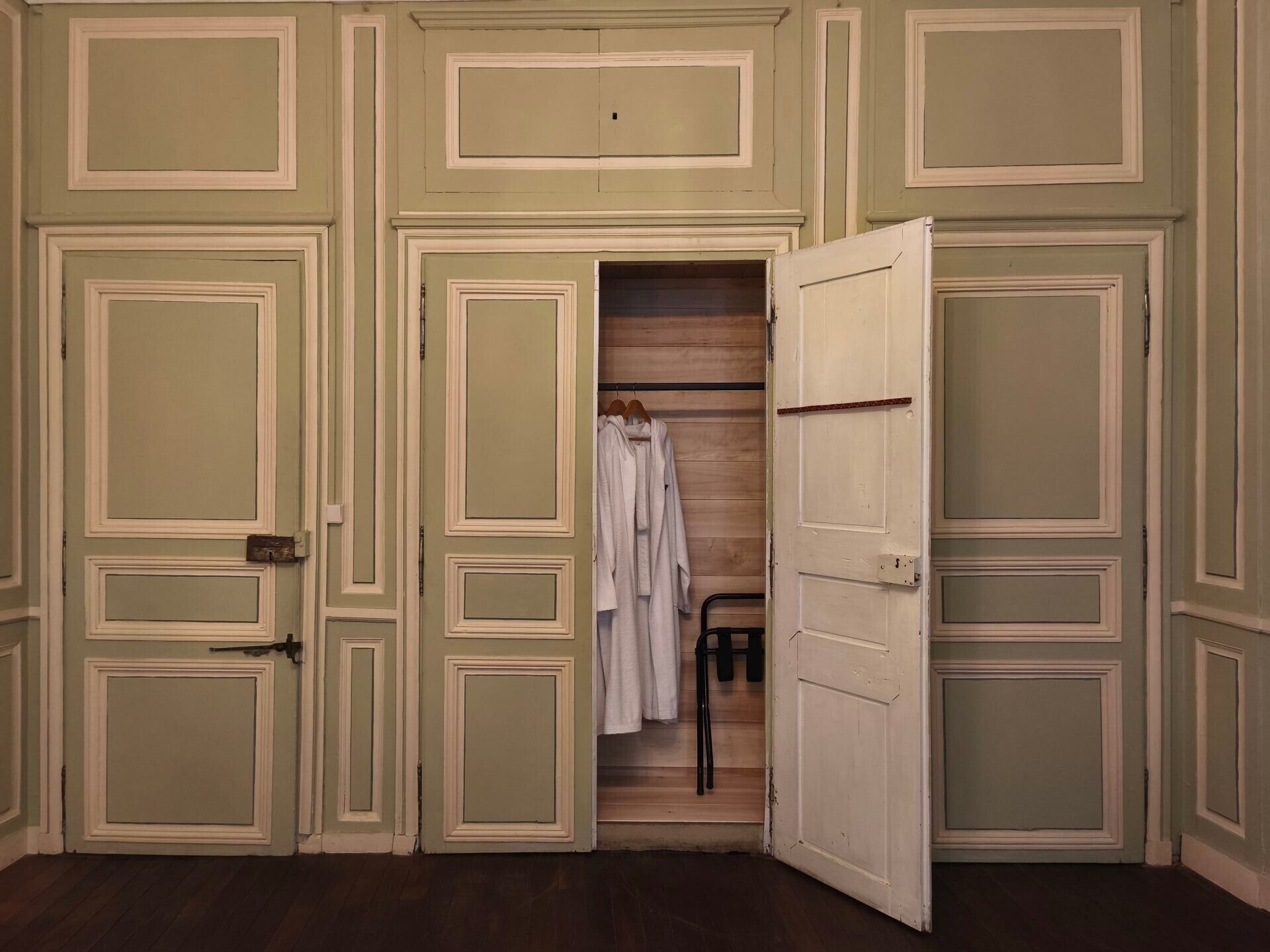 Een kamer met een houten vloer, een kledingkast met ophangrek en een deur naar een andere kamer.